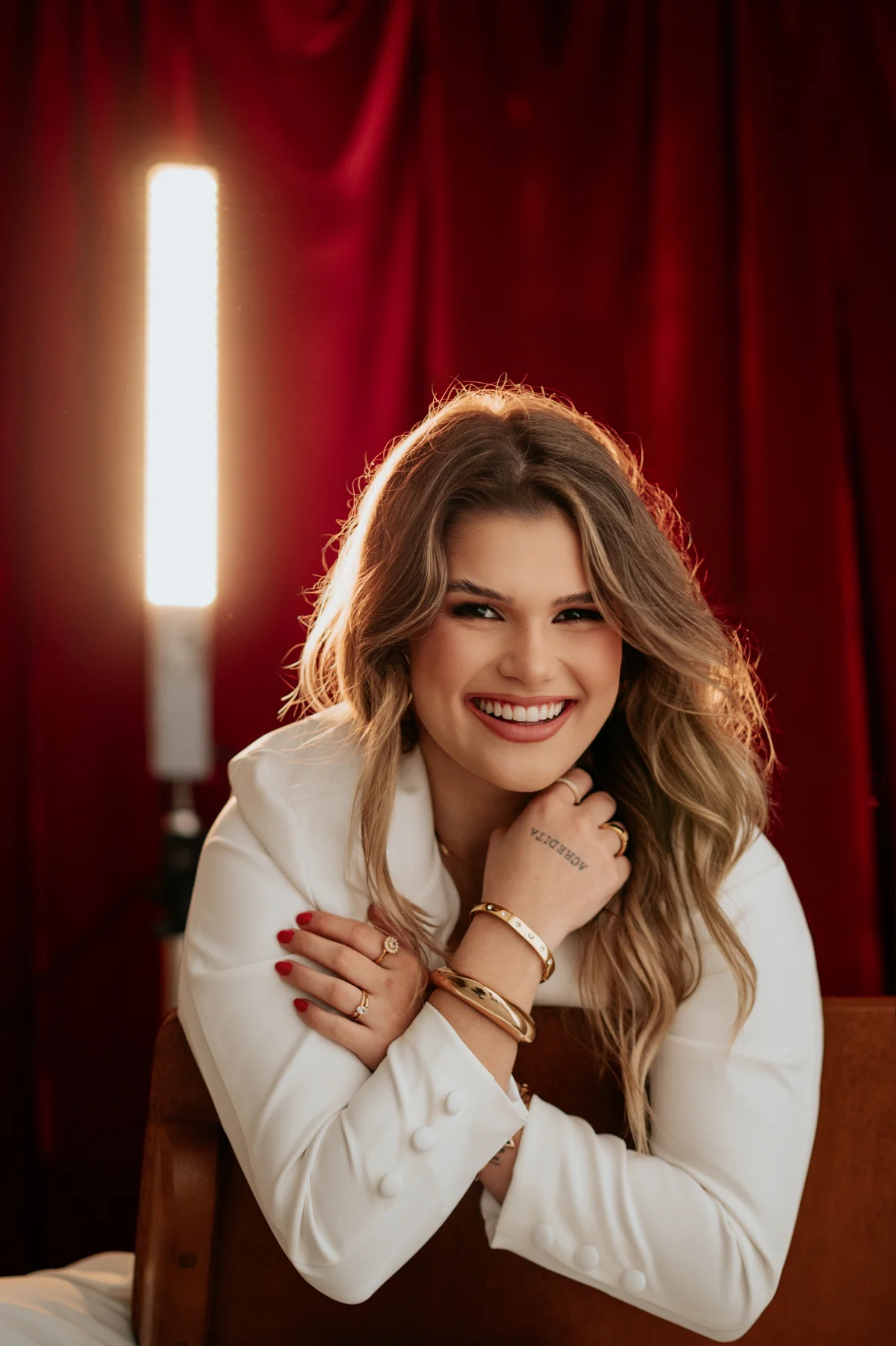 Retrato de Maria sorrindo, de roupa branca diante de uma cortina vermelha